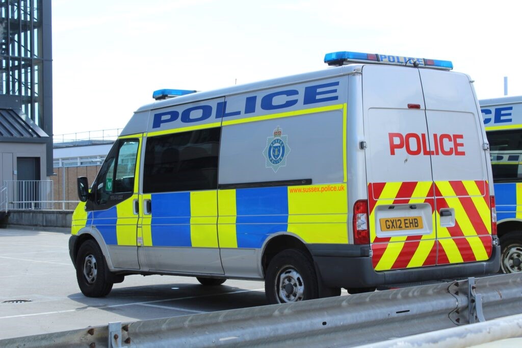 A police van seen from the rear left with a metal barrier in the foreground.
