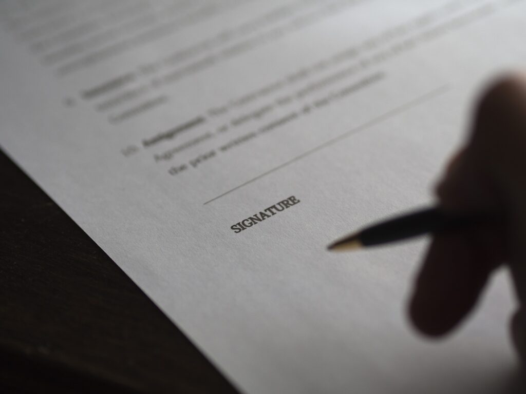 A hand holding a pen above a document reading "signature".