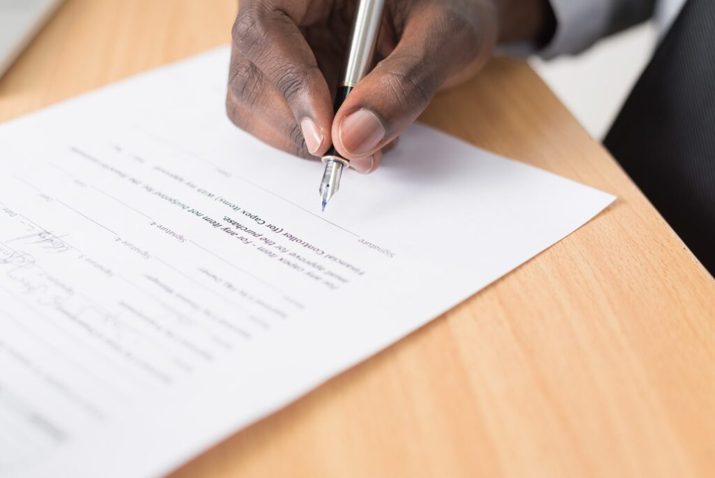A hand holding a pen about to sign a document on a wooden desk.