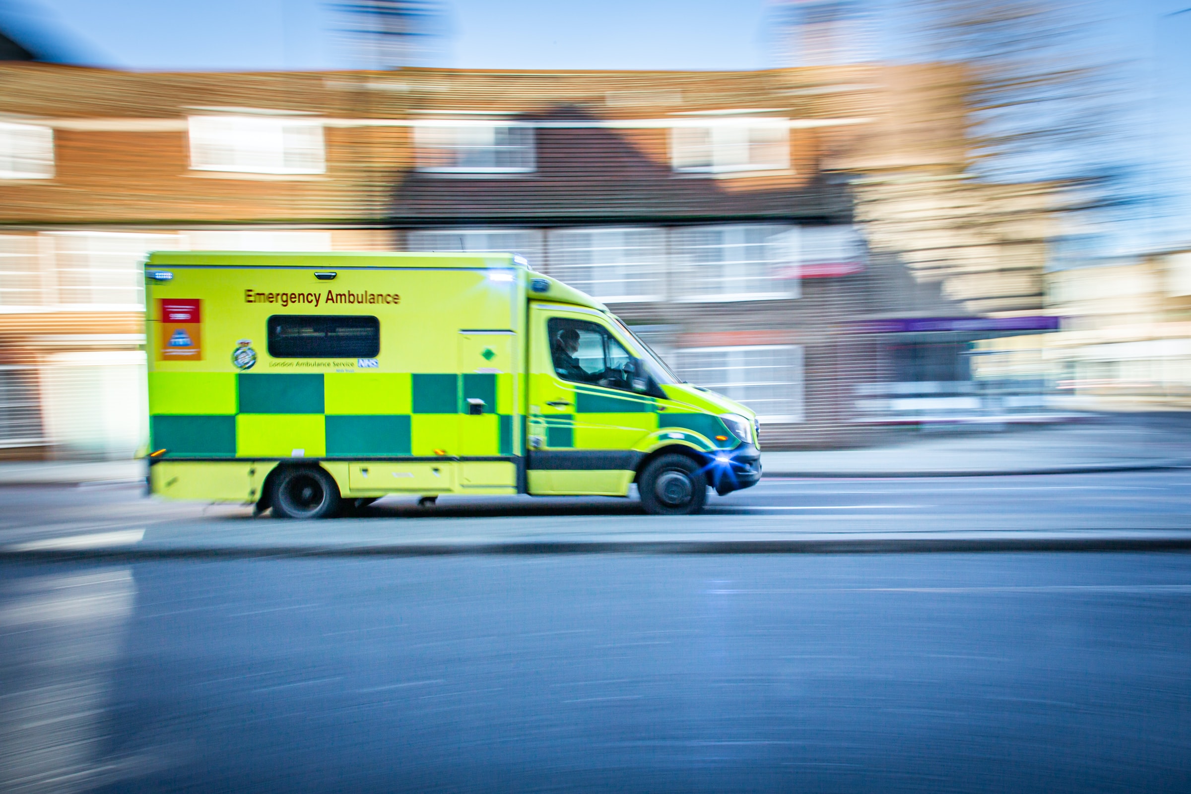 An ambulance viewed from the side with a house in the background; the image is heavily motion-blurred.