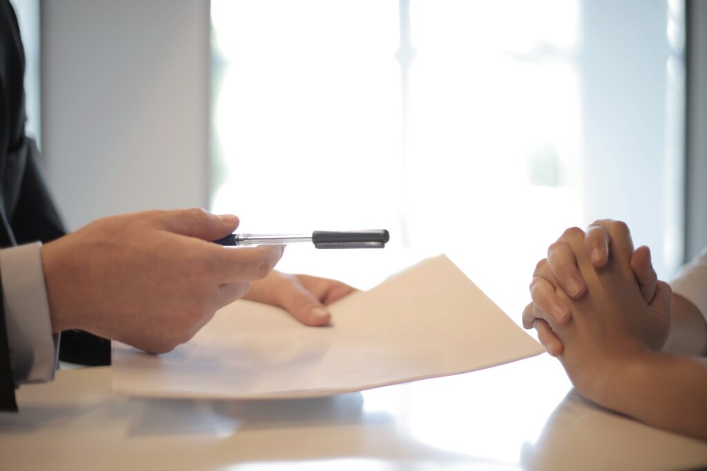 A close-up of two pairs of hands, one handing a paper and pen to the other.