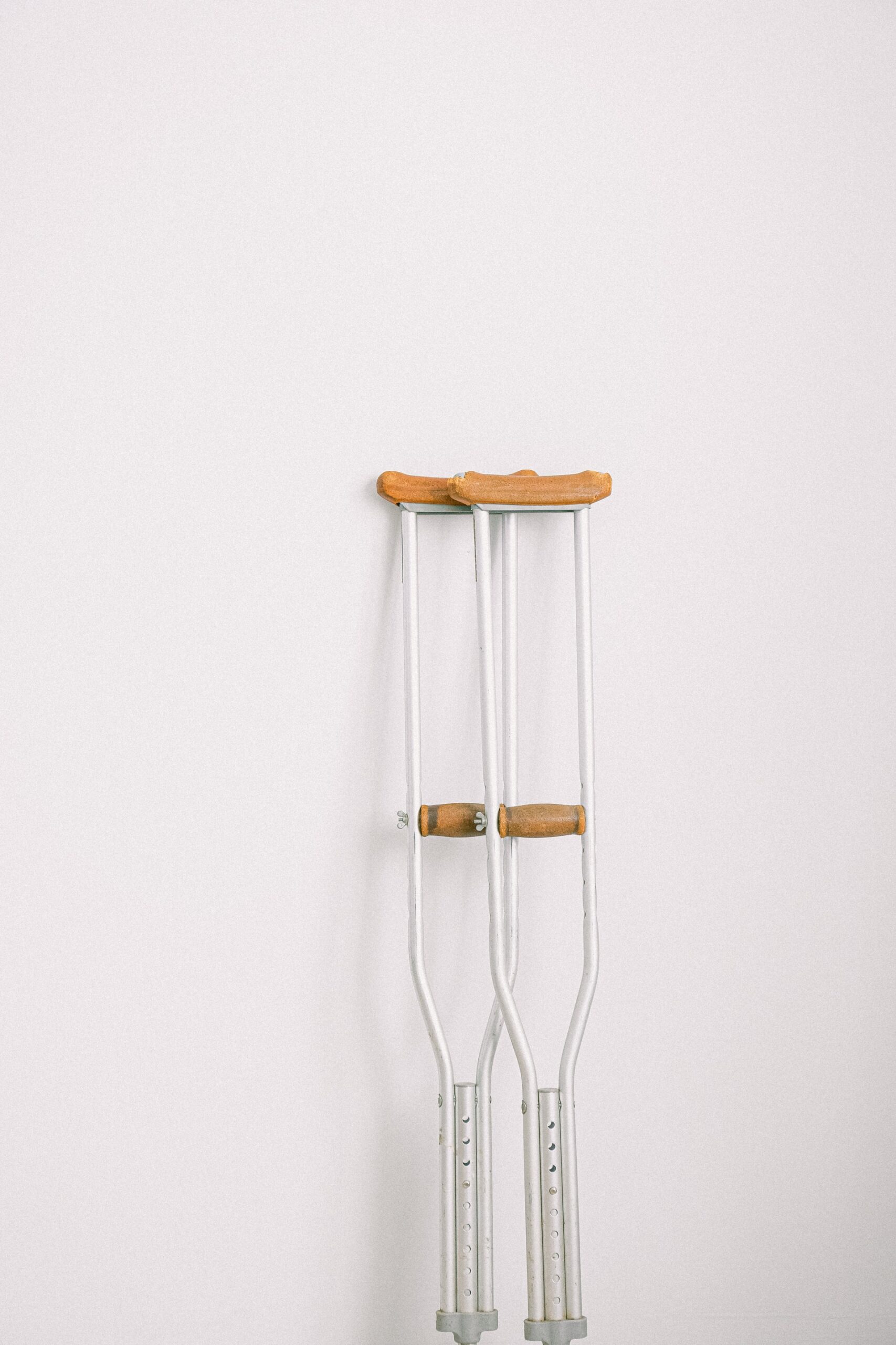 A pair of metal crutches with wooden handles against a white wall.