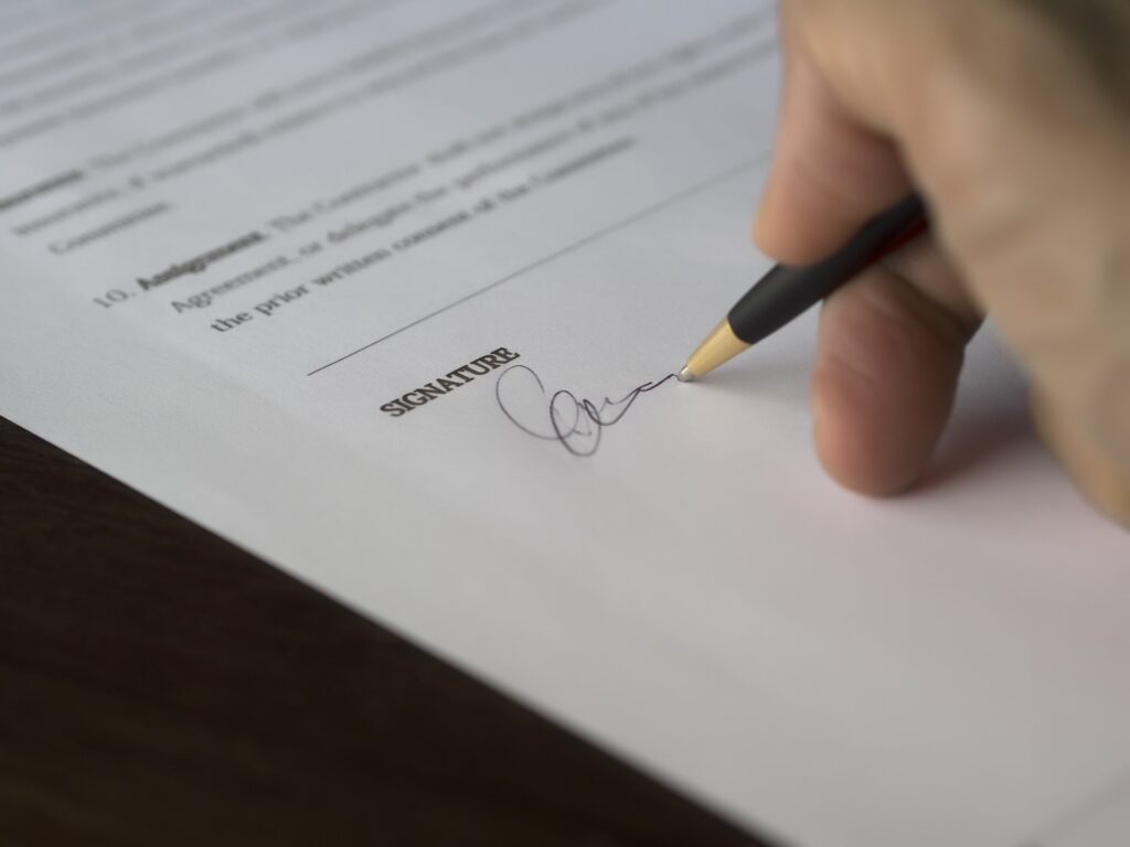 A hand signing a document with a black pen.