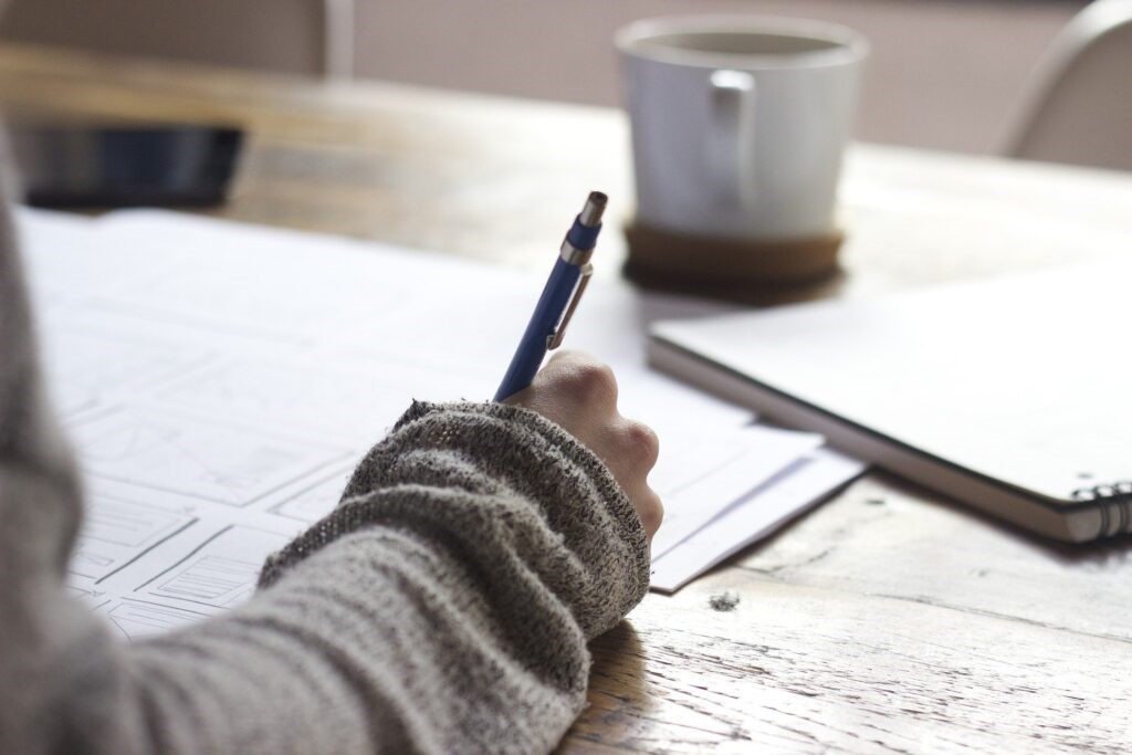 A person writing in a notebook resting on a wooden table. 