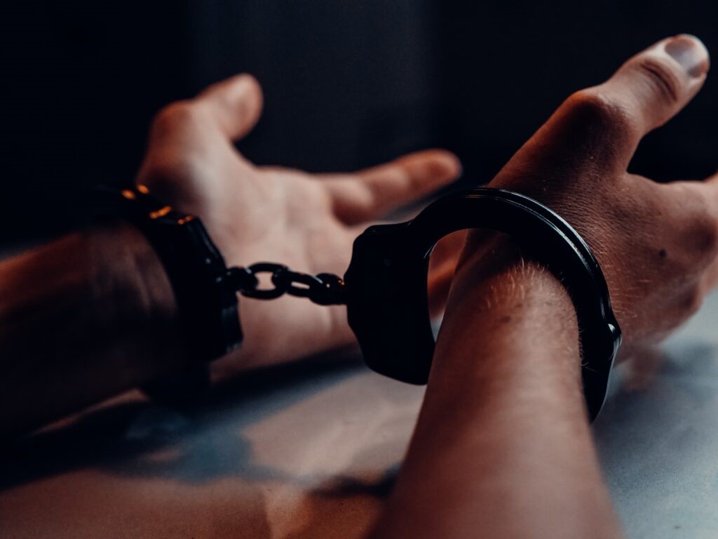 A persons hands resting on a table while in handcuffs. 
