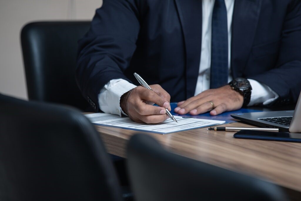 A person in a suit during a meeting signing papers.