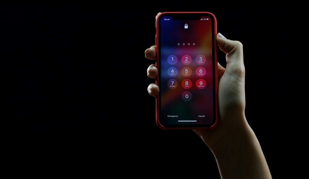 A black background with a person's hand holding an iPhone, displaying the iPhone lock screen. 