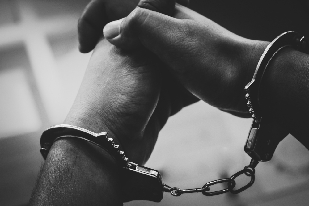 Black and white image of a persons handcuffed hands with intertwined fingers