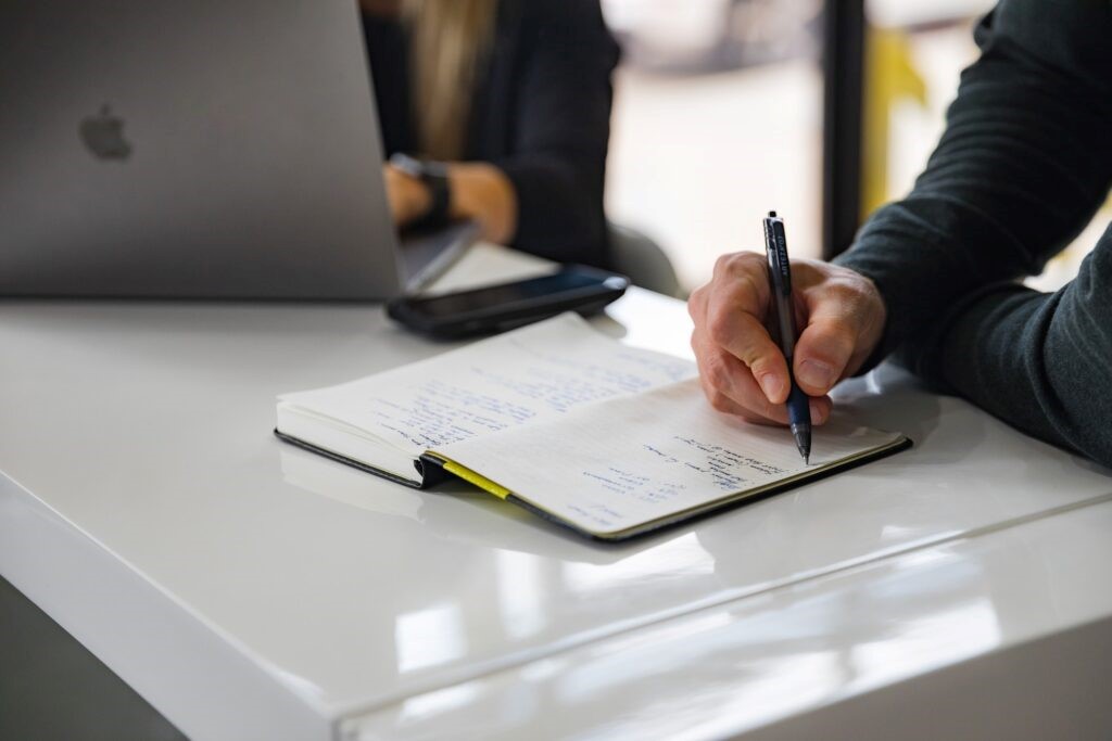 A table with two employees working on a laptop and taking notes in a notepad. 