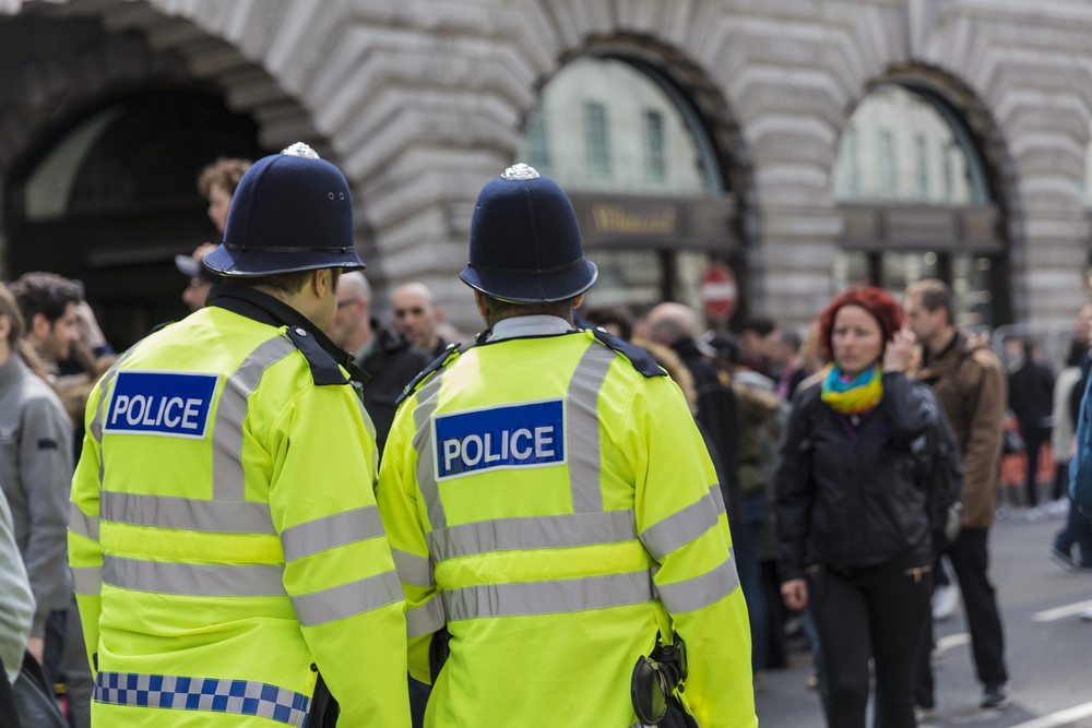 Colour image of two police officers policing an event on the streets. Th two officers are wearing hi-vis police jackets and have their backs to the camera