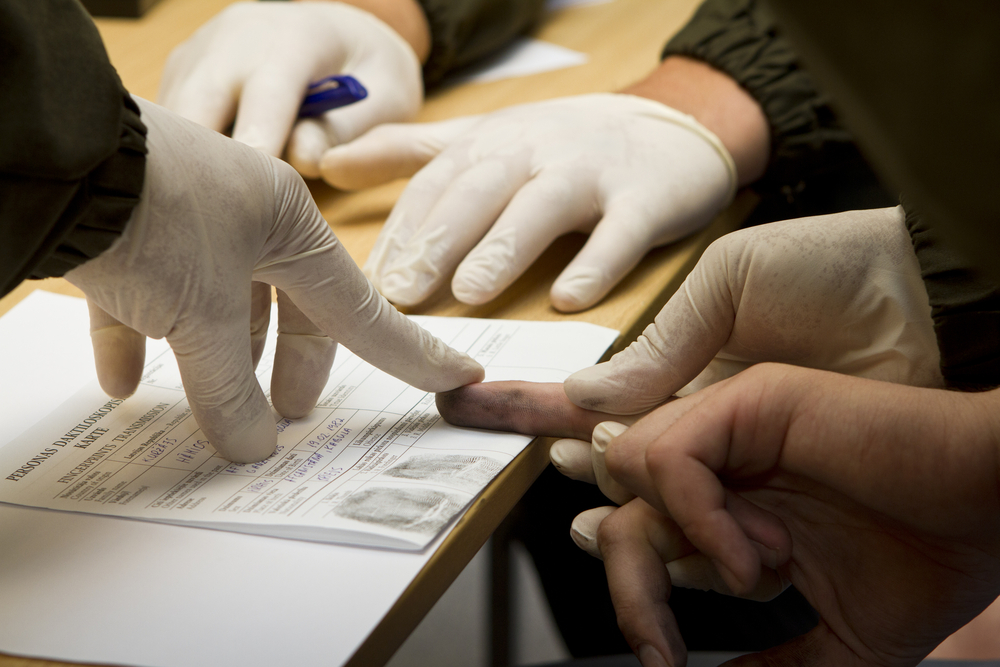 Gloved police hands take fingerprint from civilian under unlawful arrest.