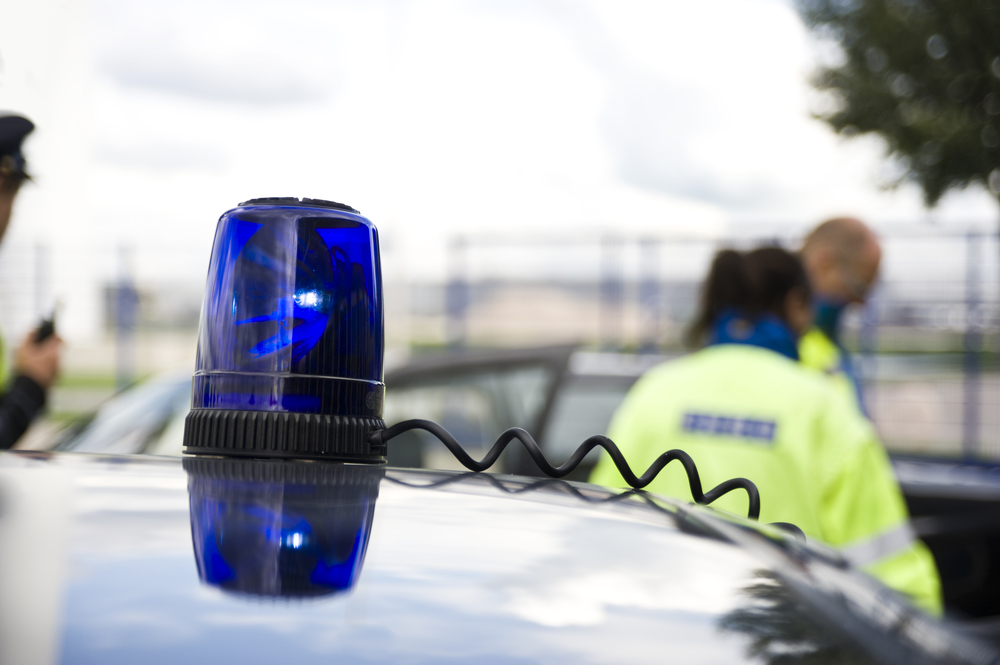 Blue light flashes on top of car with police in background for a blog outlining do you have to stop for an unmarked police car