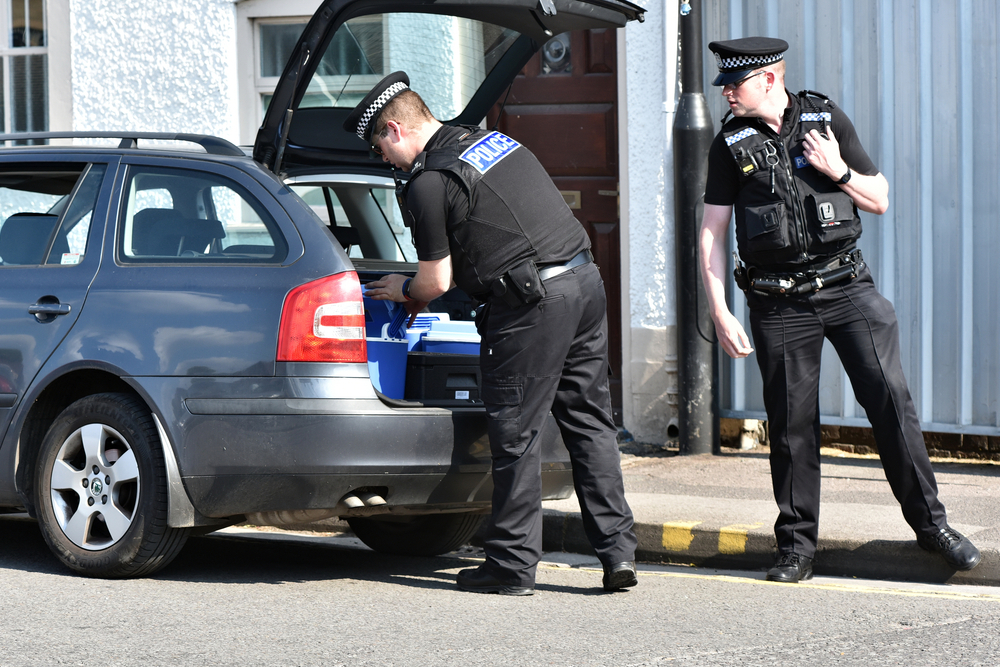 Two police officers search a car on cordoned off street for can police enter your home in the uk blog.