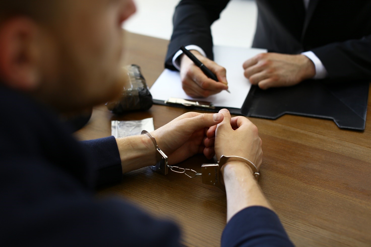 Image of a man in handcuffs being interview by a police officer who is taking notes 