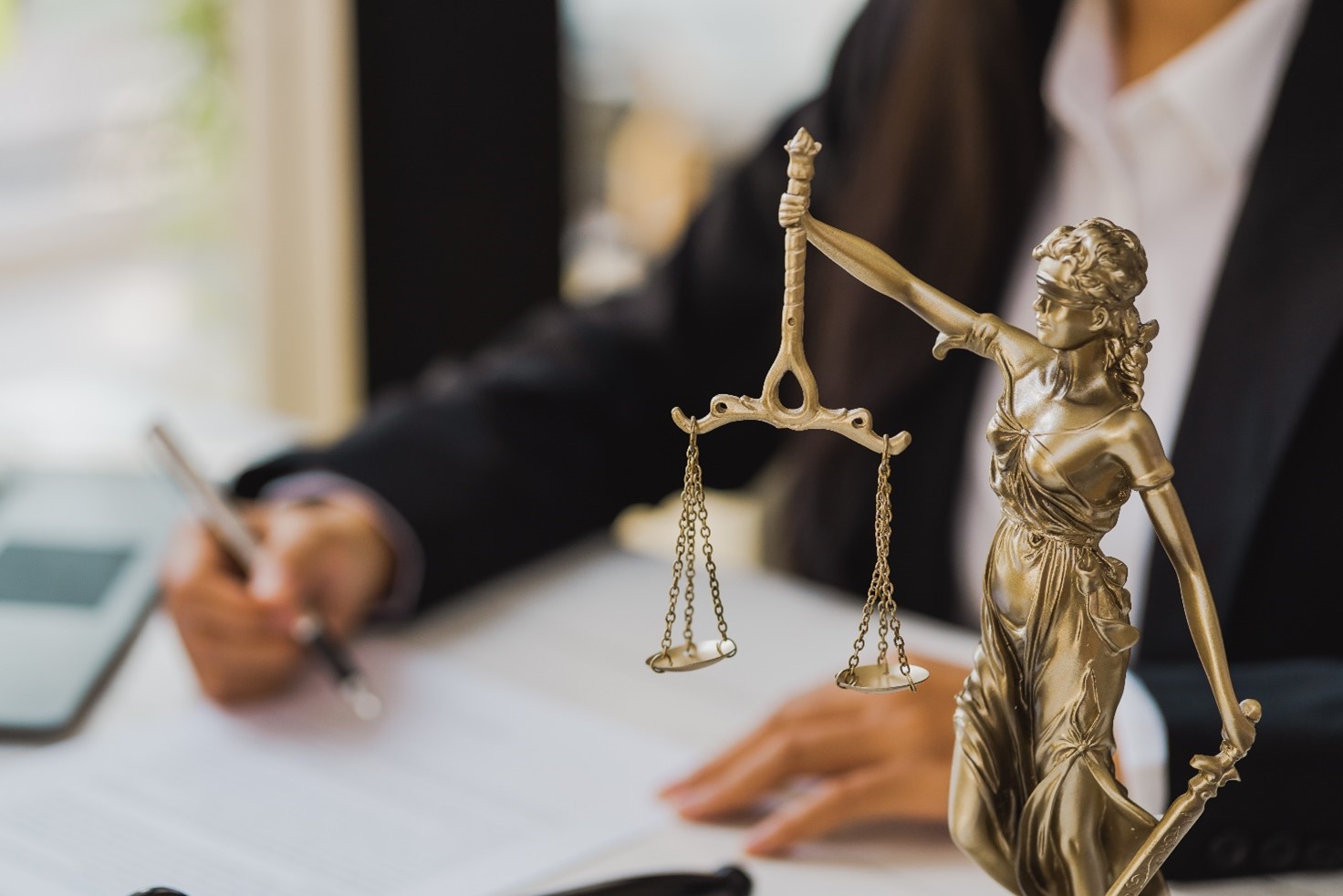 Image of a solicitor sat a desk reading a letter with pen in hand, in the foreground is a justice statue 