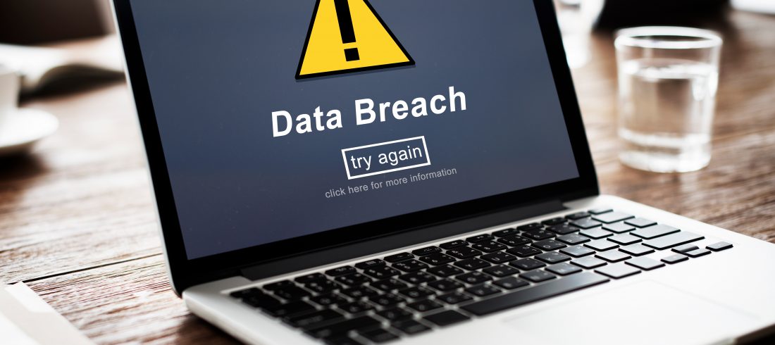 Data breach concept image, a laptop on a table with a warning symbol on screen and white text saying data breach