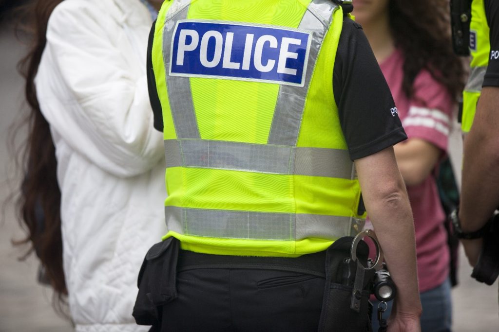 Image of the back of a police offer wearing a high-vis police vest speaking to two women on the street