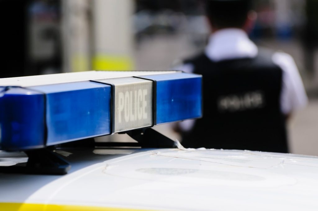 Image of a police siren on top of a police car, in the background is a police officer 