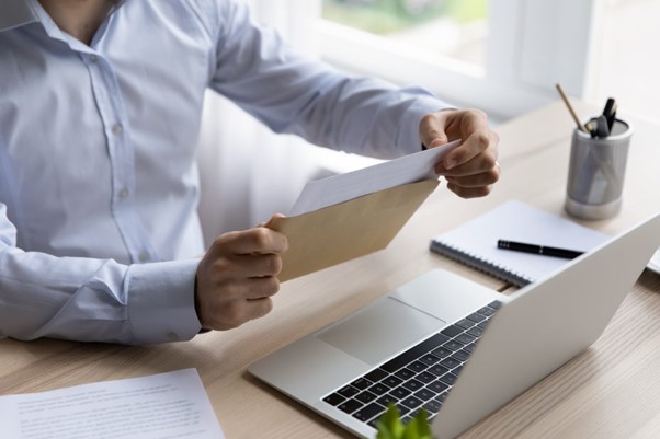 Image of a man sat behind a desk in front of a laptop opening a letter in a brown envelope