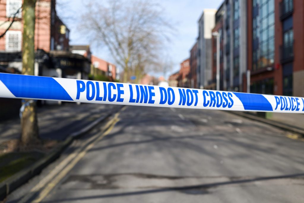 Image of police tape across a street reading 'police line do not cross' 