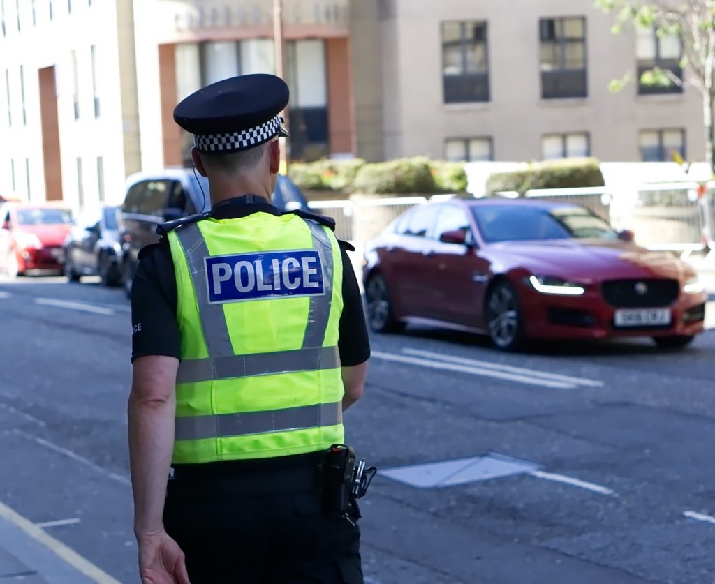 Image of a police officer wearing a high-vis vest walking down a street with cars on