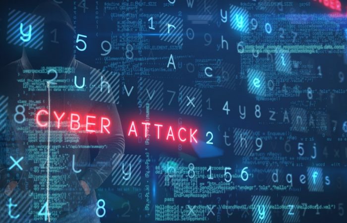 Image of a blue screen full on numbers and letters with the words 'CYBER ATTACK' written in neon red, behind the screen is a hooded man
