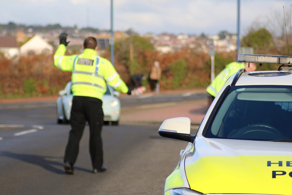 Picture of a police officer stood in the road next to a police car 