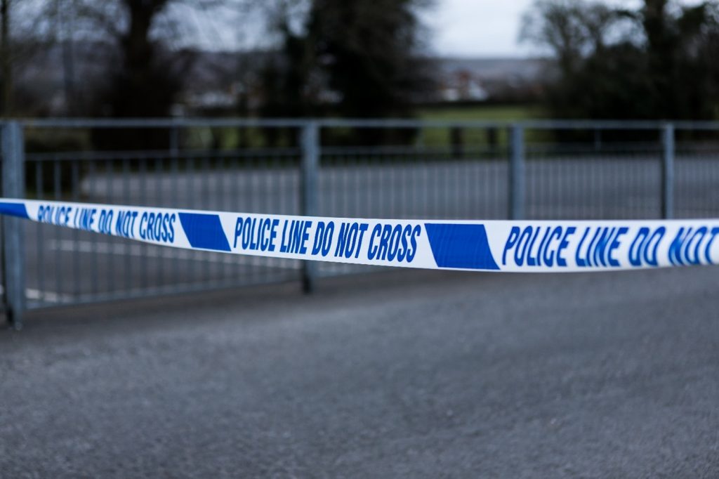 A photograph of blue and white police tape saying 'Police line do not cross' taped across an empty street.