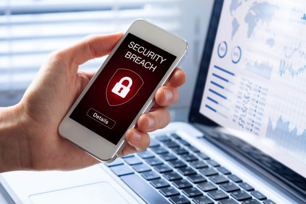 A person's hand holding a white iPhone with a security breach warning sign on the screen. 