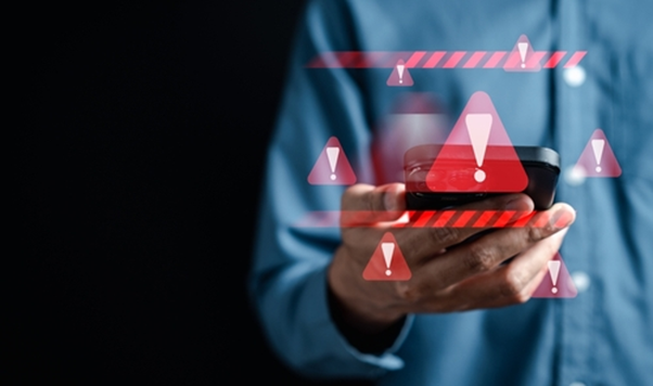 Picture of a man holding a phone with red warning symbols floating around it.