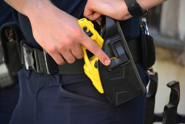 Up close picture of a police officer pulling a yellow taser out of his belt.