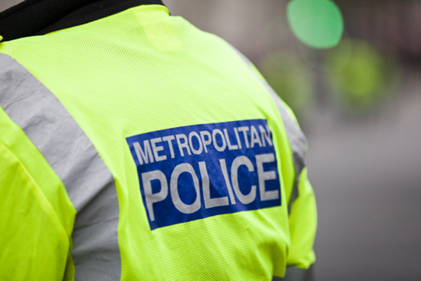 A close up image of the back of a police officer wearing a high-visibility neon green police jacket that says 'Metropolitan police' on the back 