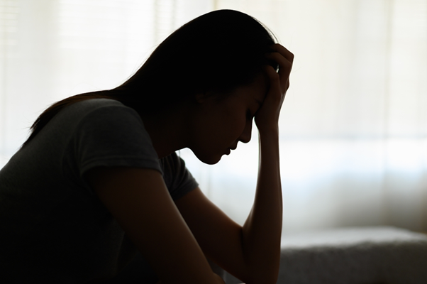 Picture of a shadowed woman looking distressed, holding her head in her hand