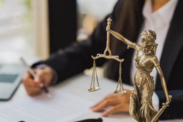 Solicitor image, a solicitor sat behind a desk writing on a piece of paper with a statue of lady justice in the foreground