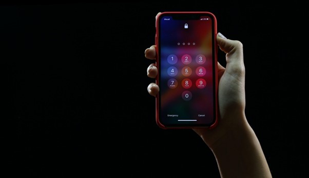 A picture of a person holding an iPhone with the lock screen asking for a password on the screen against a black background.