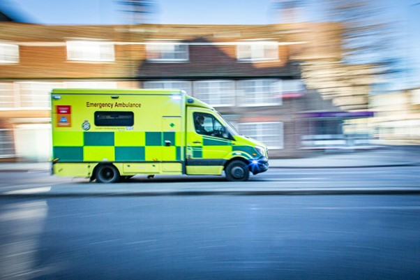 A picture of an ambulance driving fast down a street with its emergency lights on.