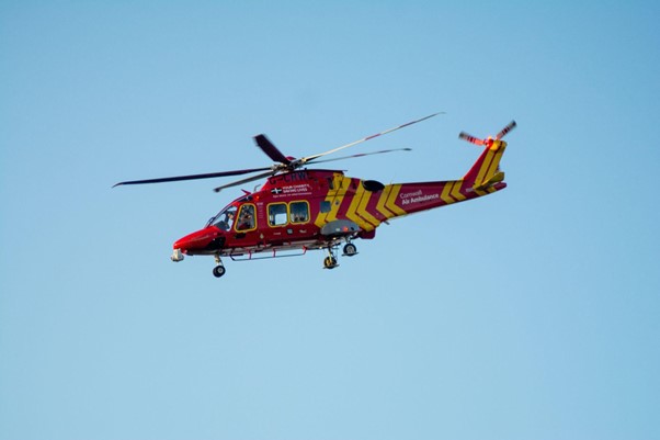 A photograph of a red air ambulance helicopter flying through a clear blue sky. 