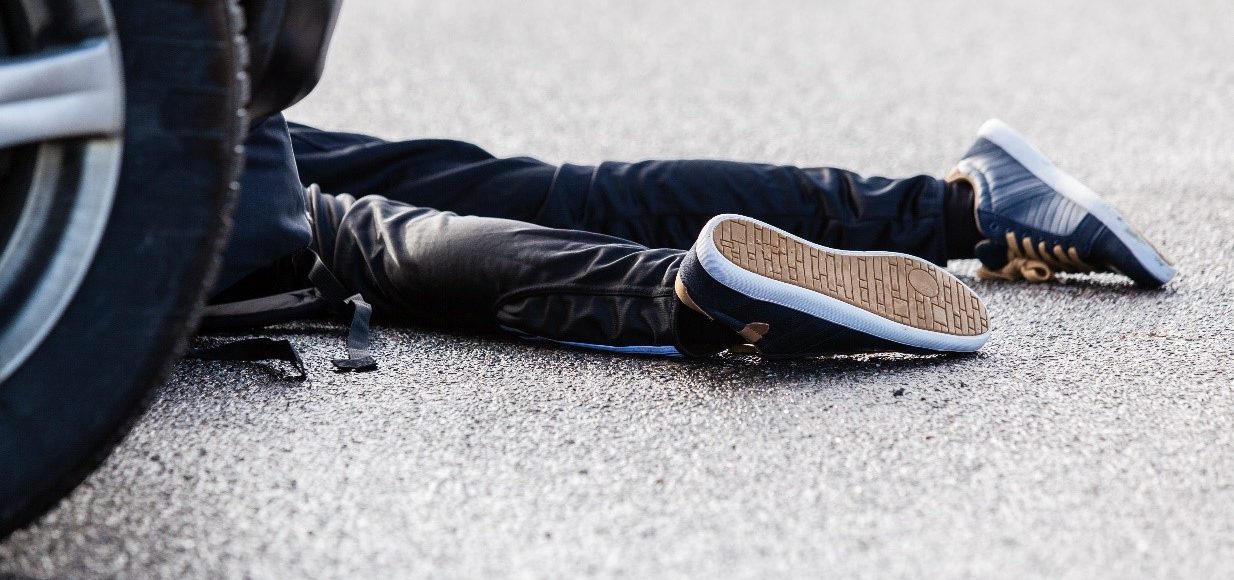 Image of a person's legs lying on the floor next to a car. Car accident concept image.