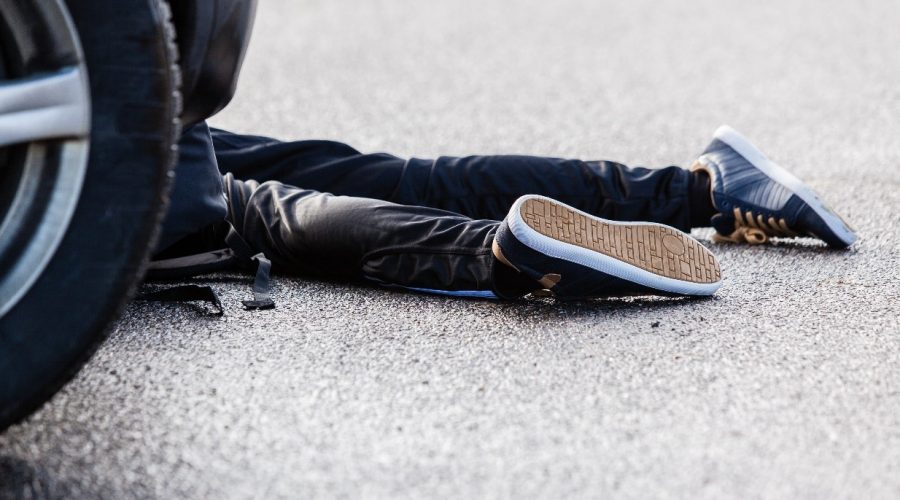 Image of a person's legs lying on the floor next to a car. Car accident concept image.