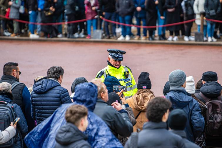 Picture of a police officer stood in front of a crowd of people outside on the street 