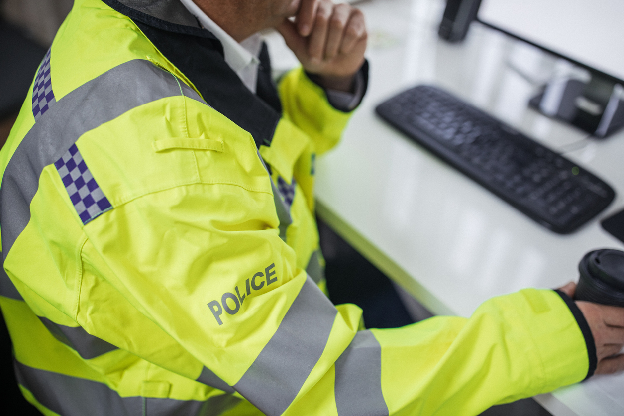 One police officer sitting at the office in front of the computer and drinking coffee