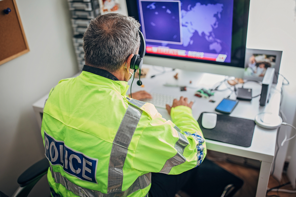 Senior British police officer with high visibility jacket and headset working on the computer in the office.