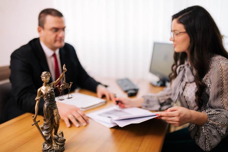 a picture of a male and female solicitors reviewing documents behind a desk. In the forefront is a statue of lady justice