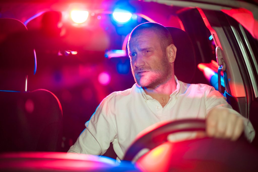 A man driving looking at the police car lights in his rearview mirror