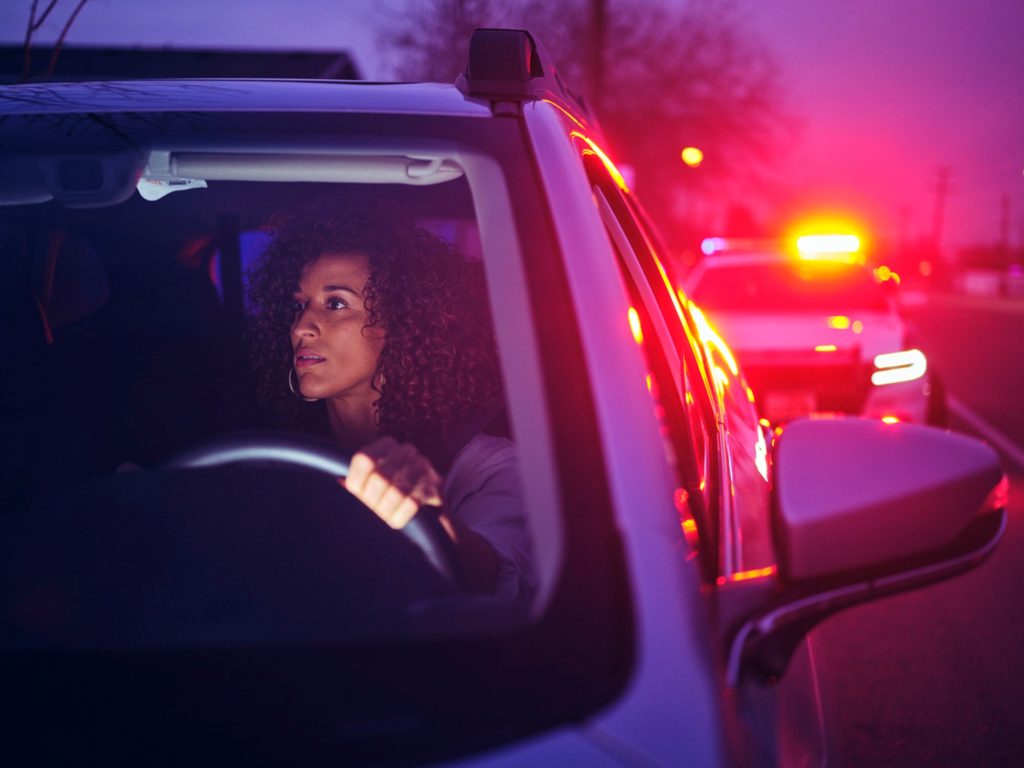 A woman getting pulled over by a police car while driving at night