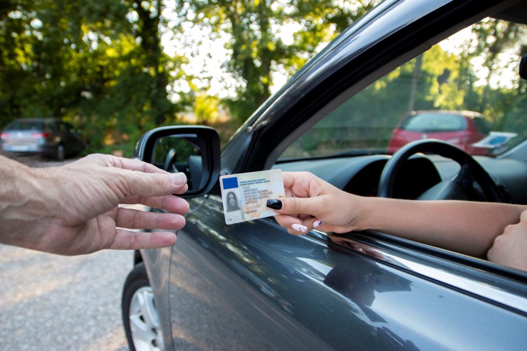 A woman handing her driving license to a police officer through the window of her car