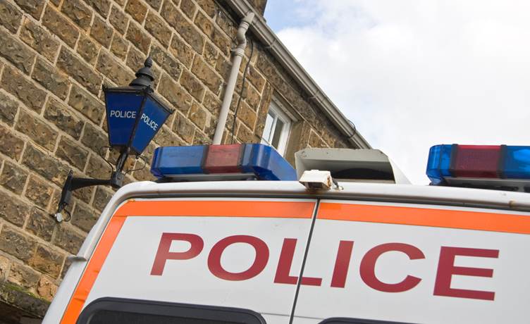 Picture of the top of a police van parked outside a police station with a blue police light outside