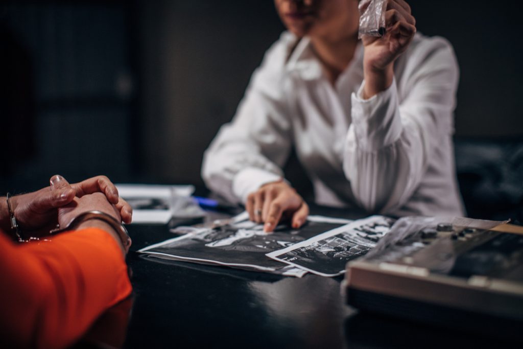 Prisoner in orange jumpsuit with handcuffs and female detective sitting in the investigation room