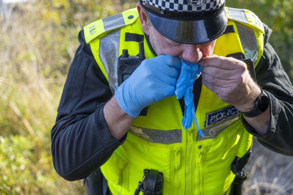 UK police officer putting on surgical gloves to avoid contaminating evidence.
