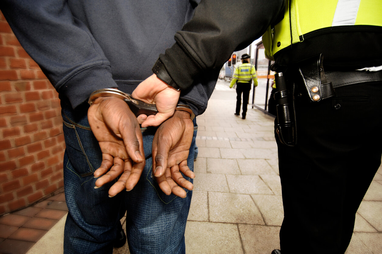 A picture of a man being arrested by police, his hands are behind his back in handcuffs and he's being escorted down the road by a police officer in uniform 